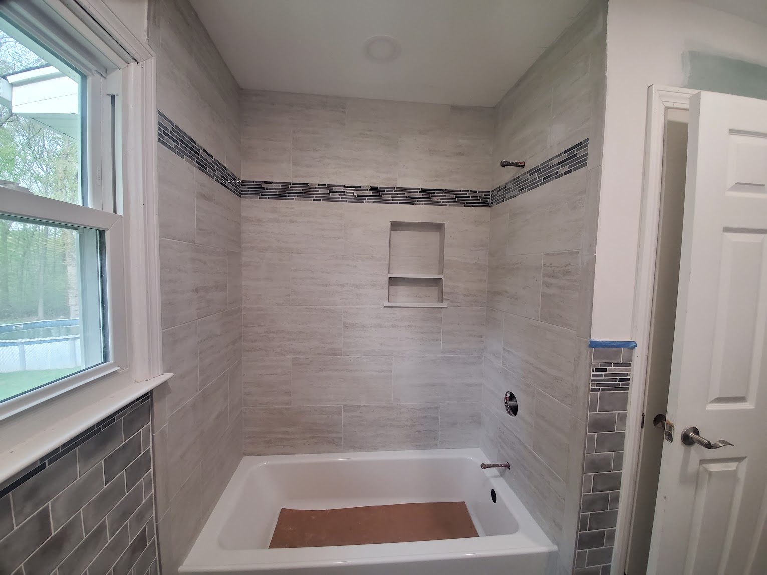 Trumbull bathroom with a tiled tub surround, inset niche, and contrasting accent band